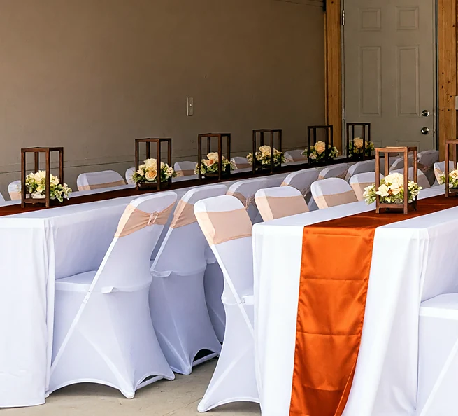 Event hall with white table covers and orange runners set by Ponnus Caters & Events